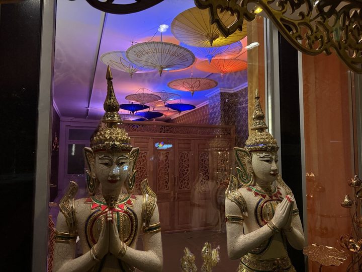 Tempelfiguren am Schaufenster, dahinter die Schirmdecke aus Chiang Mai